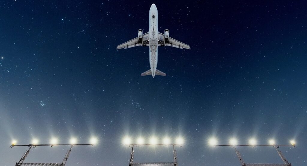 An airliner flies over runway approach lights at night