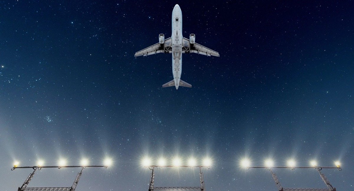 An airliner flies over runway approach lights at night